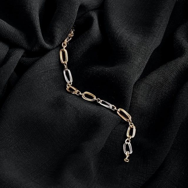 Ett tvåfärgat kedjearmband i guld och silver på svart tyg.