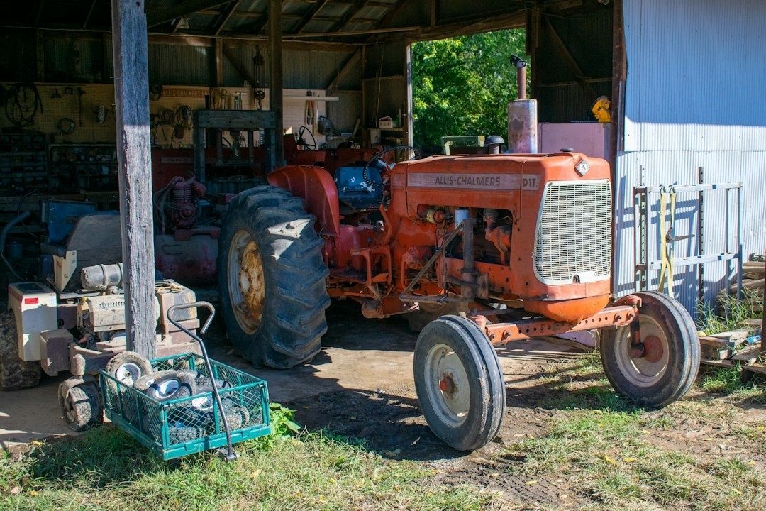 Orange Allis-Chalmers-traktor framför en verkstad med lantbruksutrustning